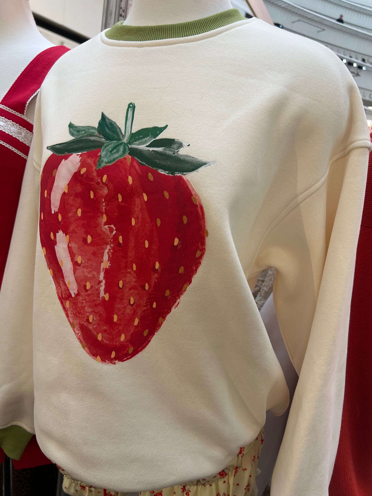 White sweatshirt featuring a large strawberry print, perfect for casual wear in the spring or summer.