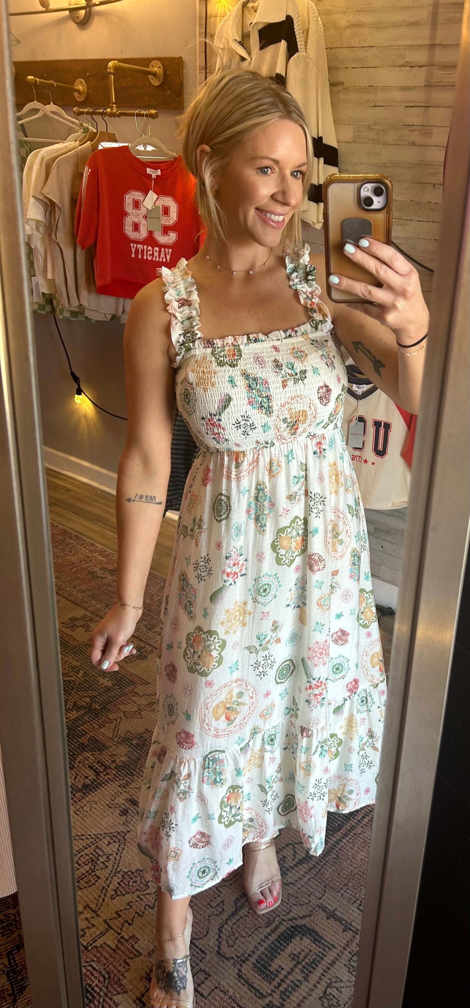 Smiling woman in a patterned dress with ruffled straps, posing in front of a mirror.