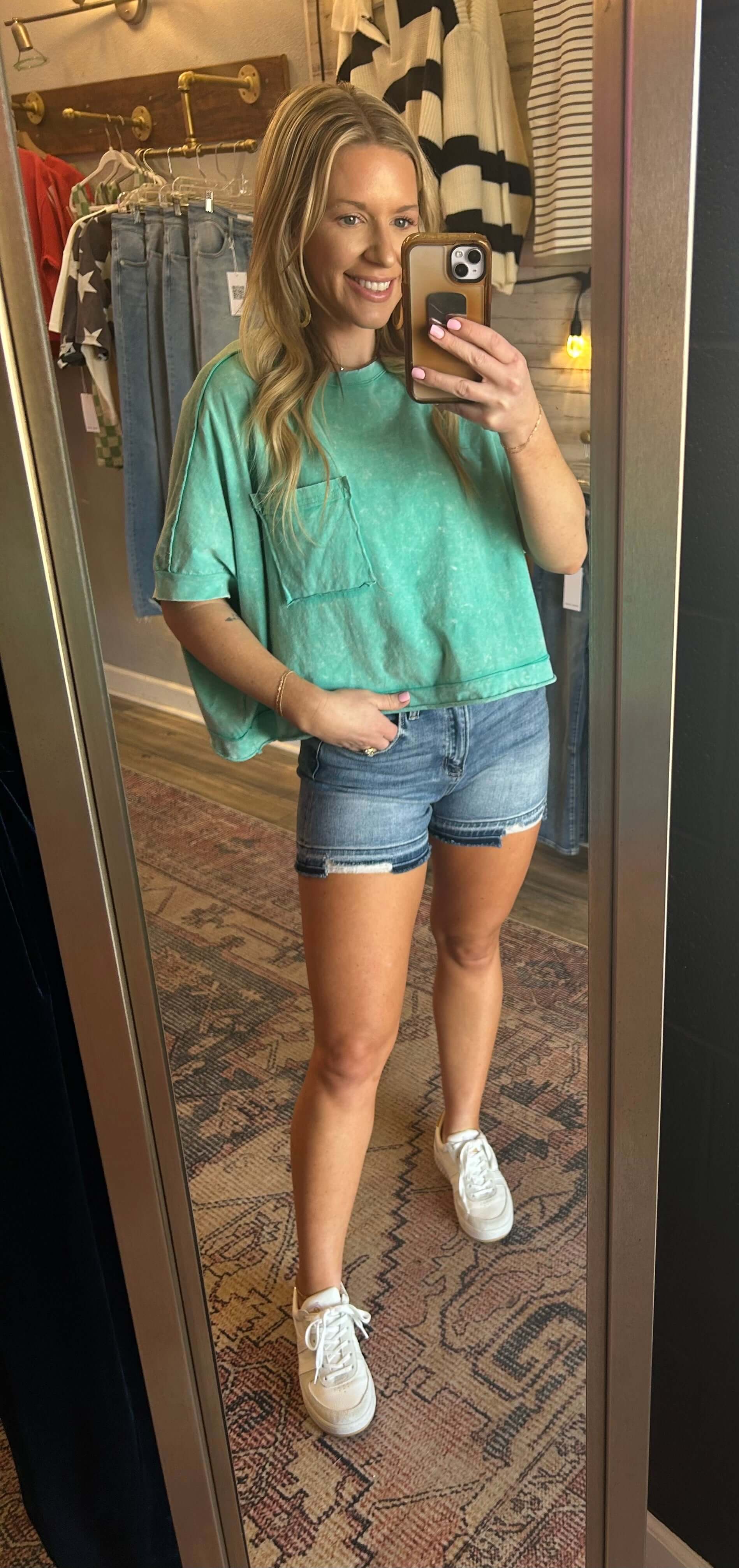 Model wearing a Mineral Wash Crop Tee with front pocket detail, paired with denim shorts and sneakers in a stylish setting.