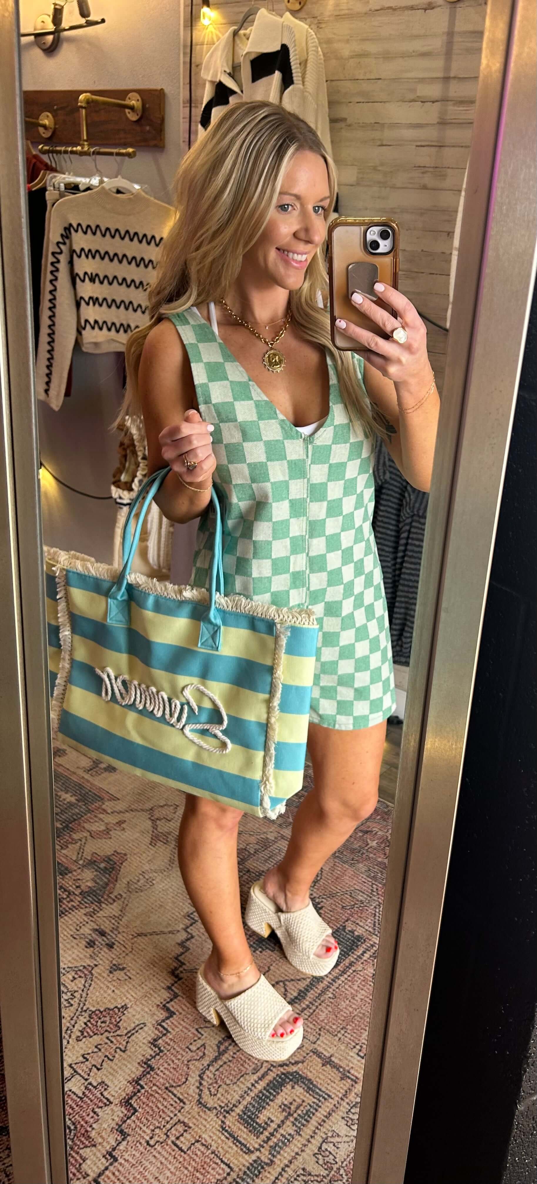 Model wearing a checkered evergreen romper with a V neck, holding a striped bag, showcasing summer fashion.