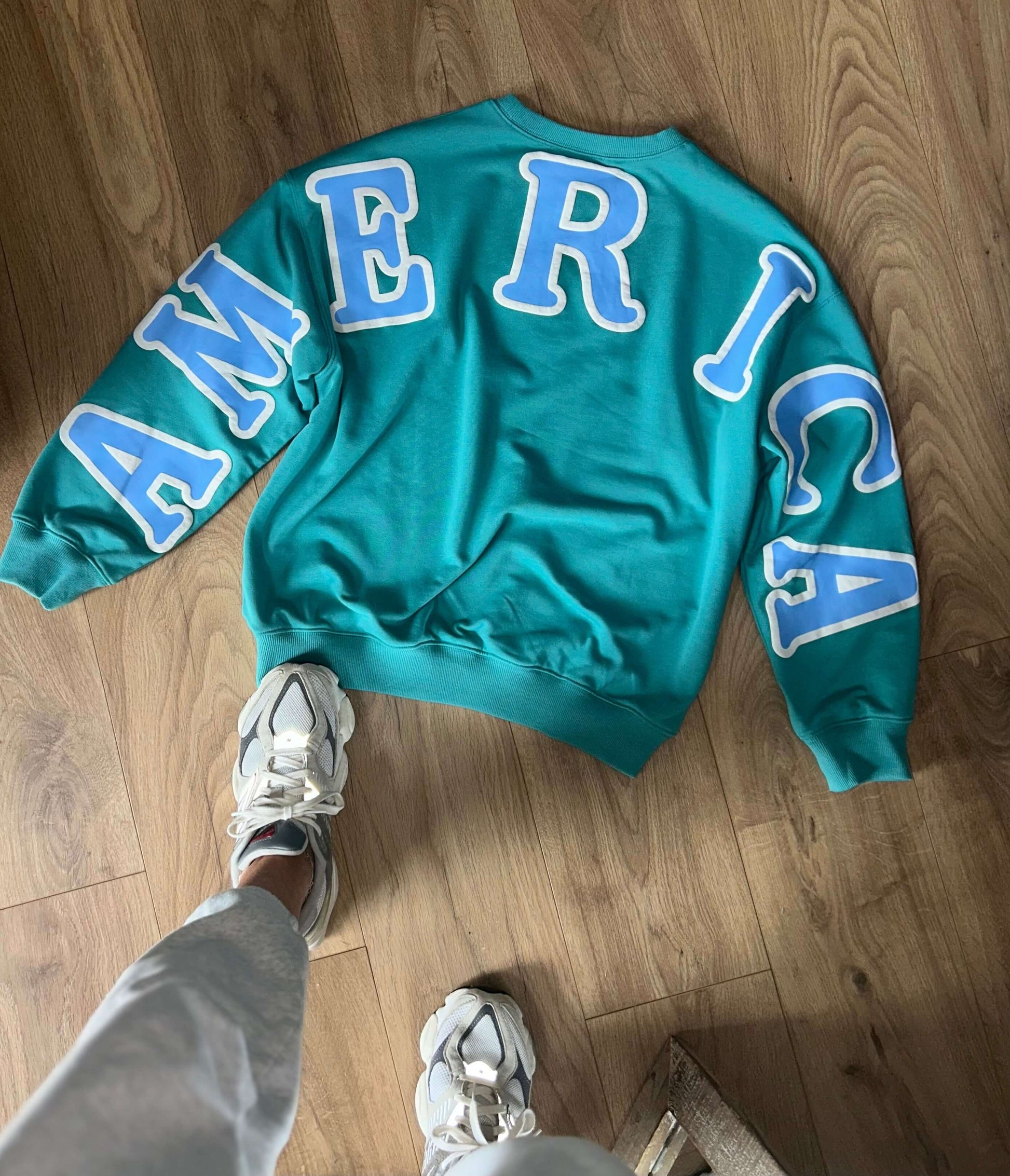 Emerald long sleeve pullover featuring 'AMERICA' on the back, perfect for spring and summer fashion.