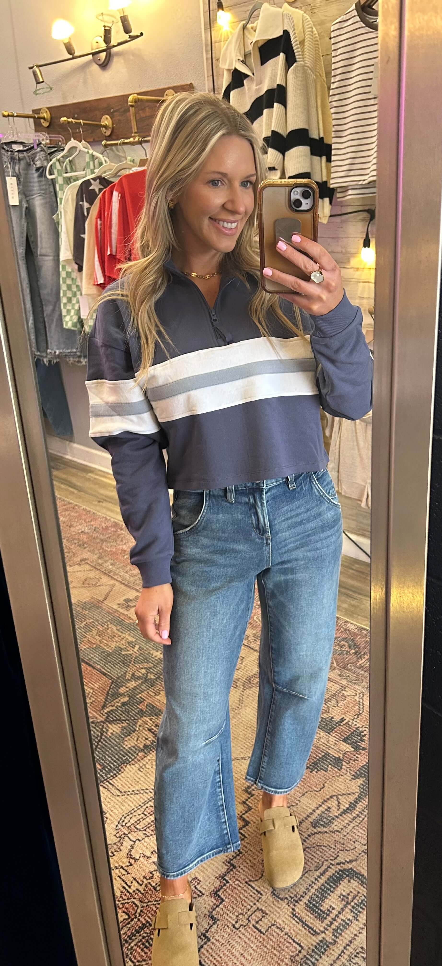 Woman wearing navy cropped pullover with stripes and high-rise loose fit cropped barrel jeans in a clothing store mirror.