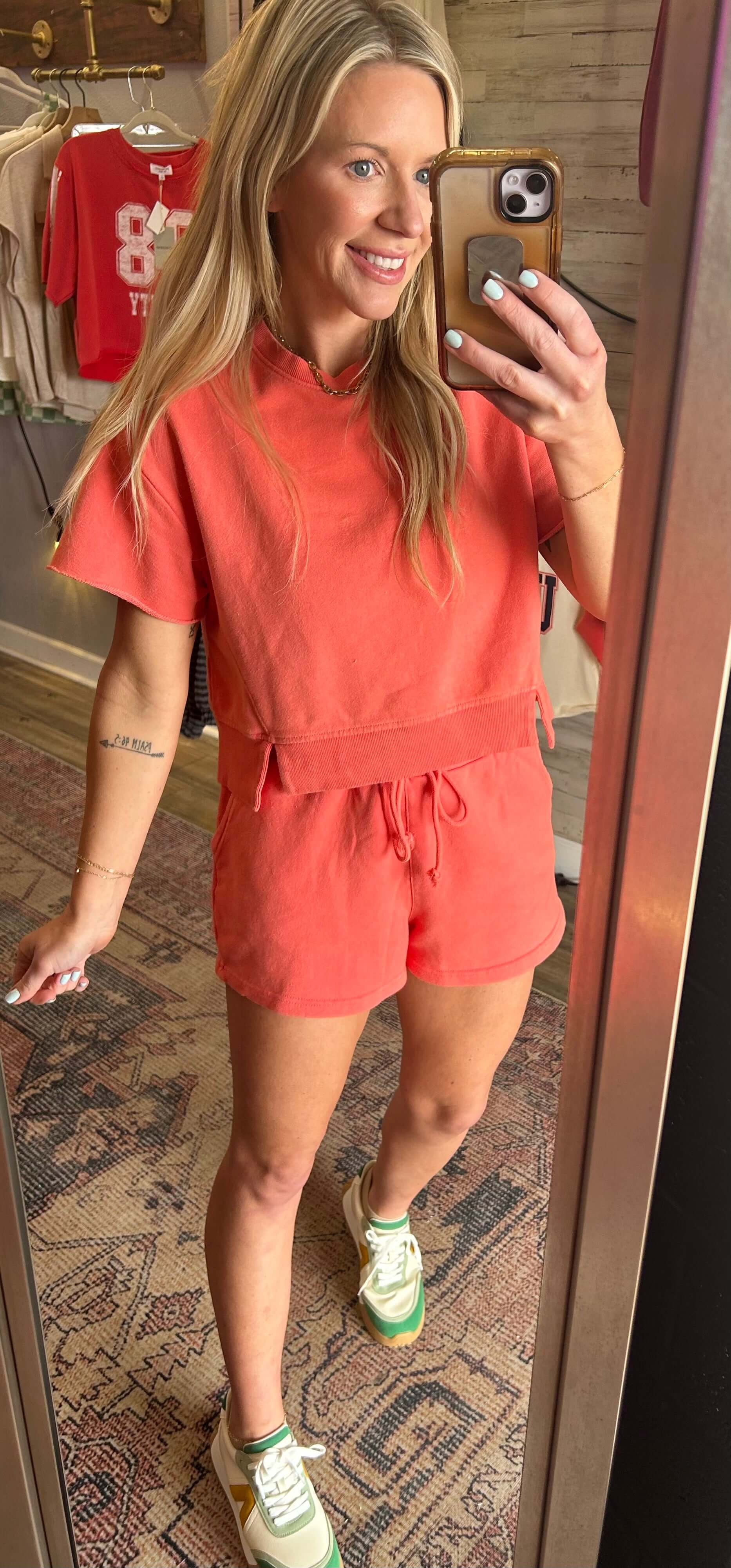 Model wearing a coral Summer Sunset 2pc short set with raw hem details and drawstring waist shorts, smiling in a mirror.