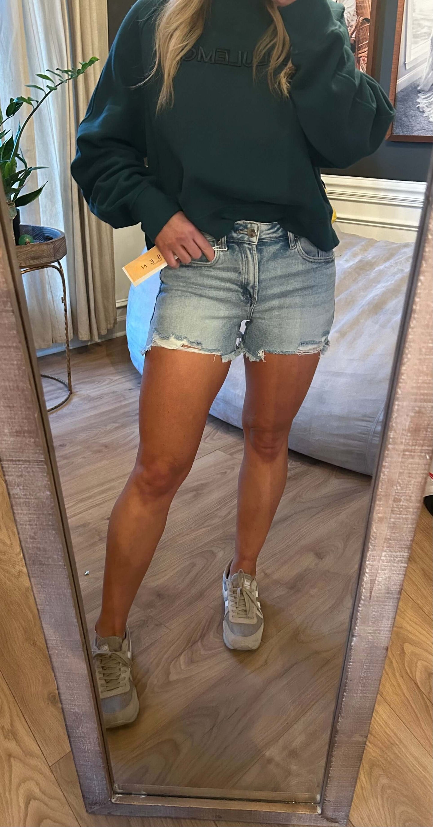 Model wearing Risen Highrise Peek-a-Boo Lining denim shorts with a green sweatshirt in front of a mirror.