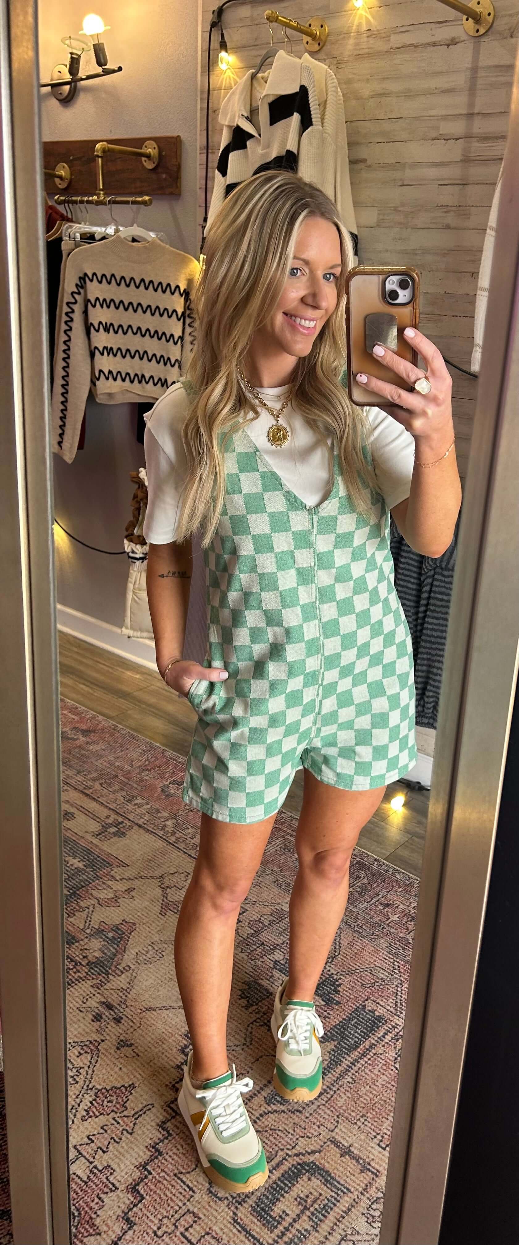 Model wearing a checkered evergreen romper with V neck, side zip closure, paired with sneakers, in a bright and stylish room.
