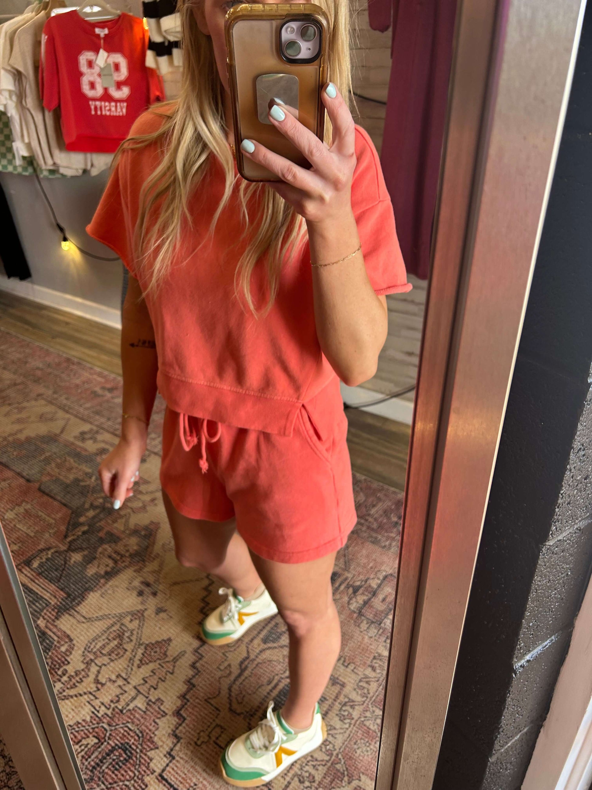 Model in a coral 2pc short set featuring a cropped top and drawstring shorts with pockets, standing in front of a mirror.