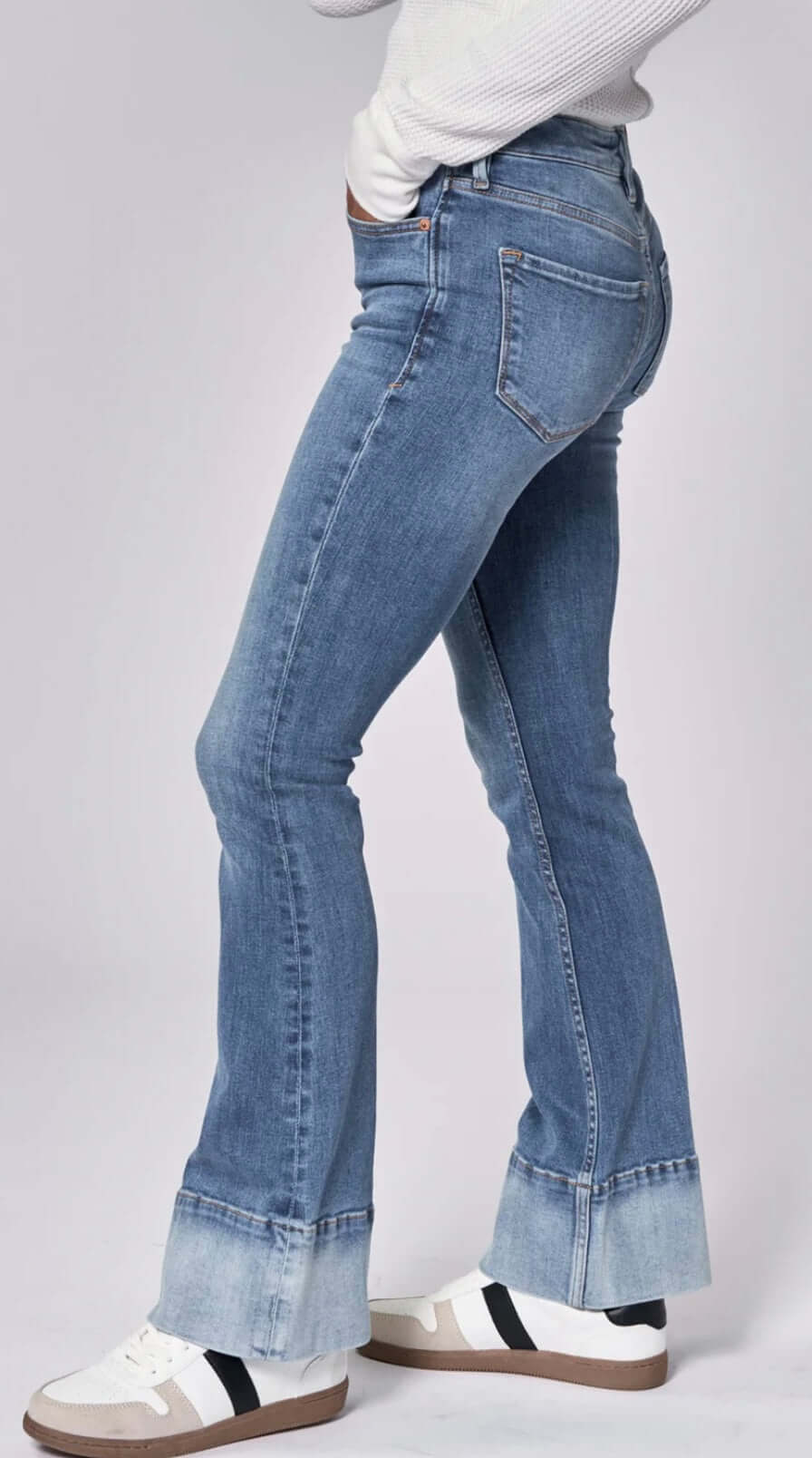 Side view of women's Jaxtyn mid-rise bootcut jeans in lagoon with a stylish contrast hem band and casual sneakers.