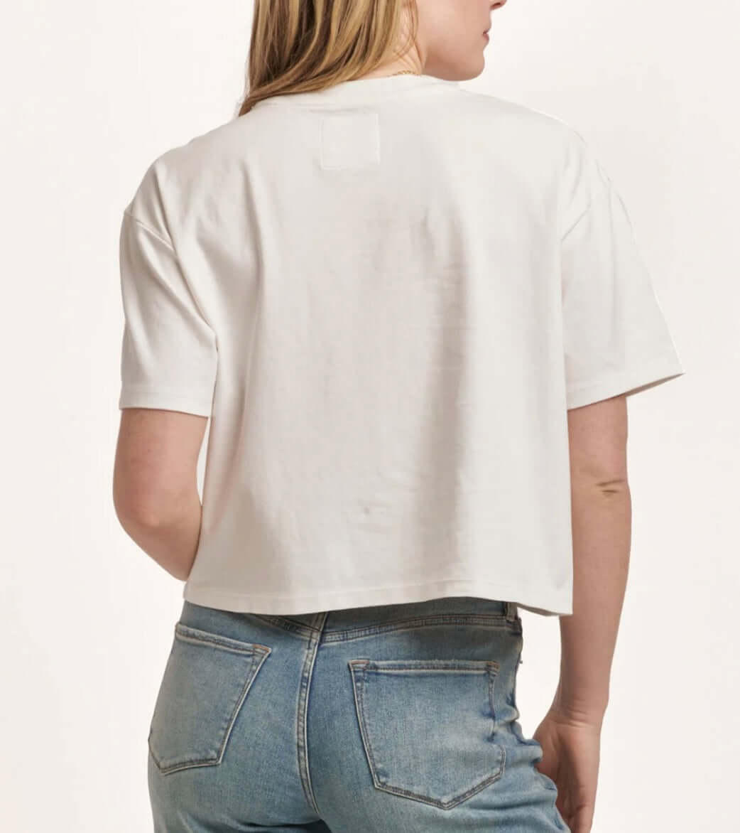 Back view of a woman wearing a white short-sleeve boyfriend jersey top, paired with blue jeans.