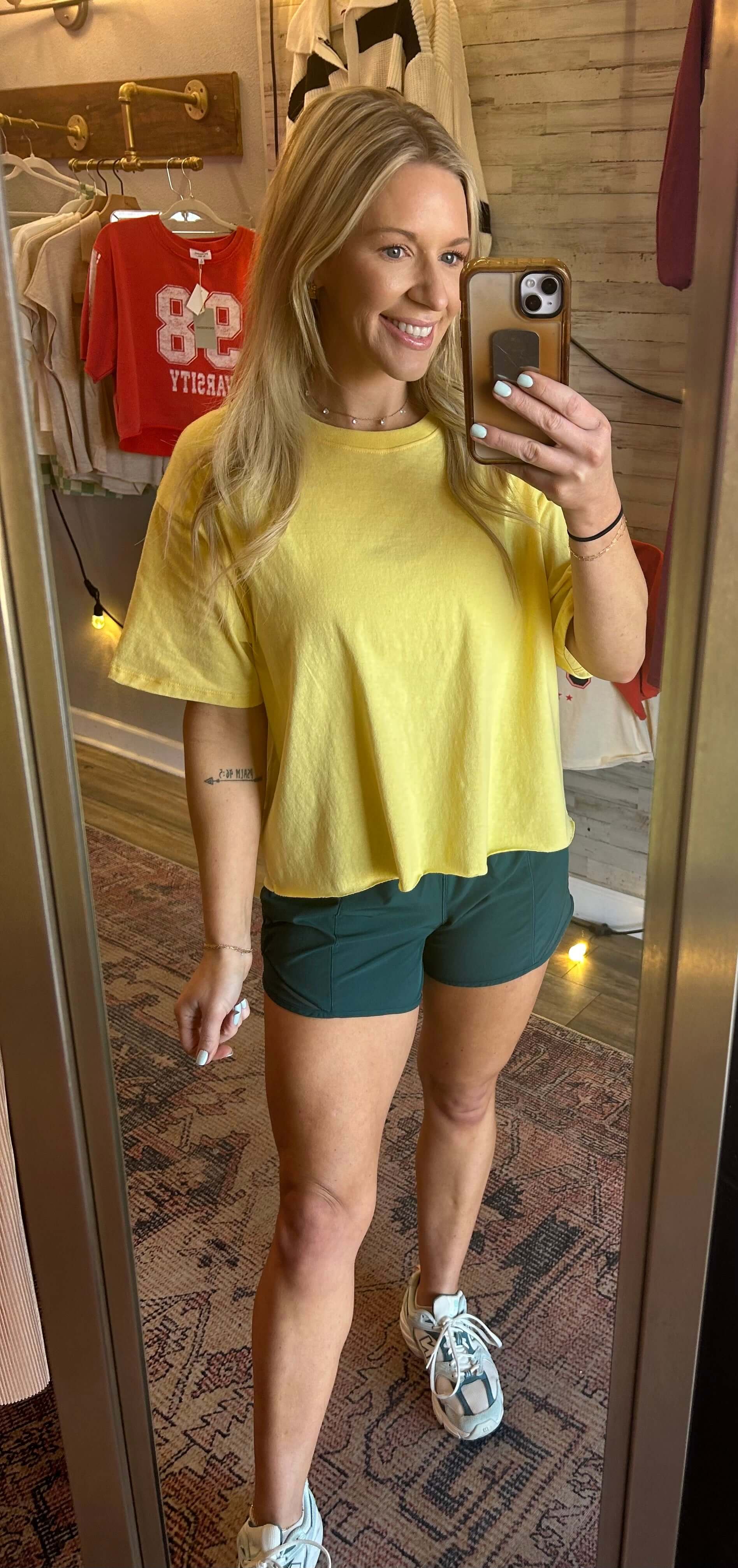 Woman wearing a yellow raw hem tee with green shorts, showcasing a casual summer outfit in a mirror reflection.