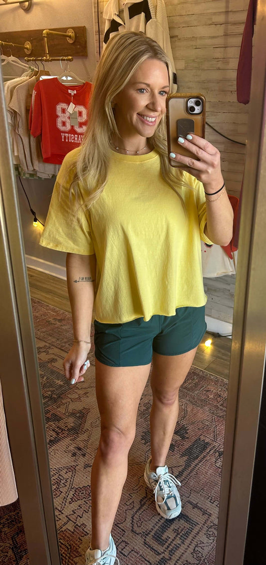 Woman wearing a yellow raw hem tee with green shorts, showcasing a casual summer outfit in a mirror reflection.