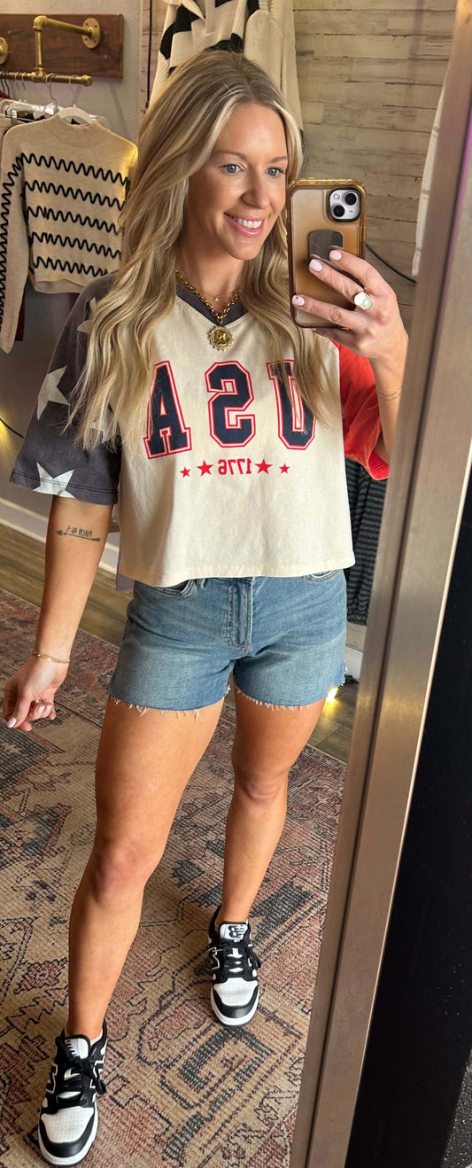 Model wearing USA raglan sleeve crop tee with star sleeve details, paired with denim shorts, perfect for summer.